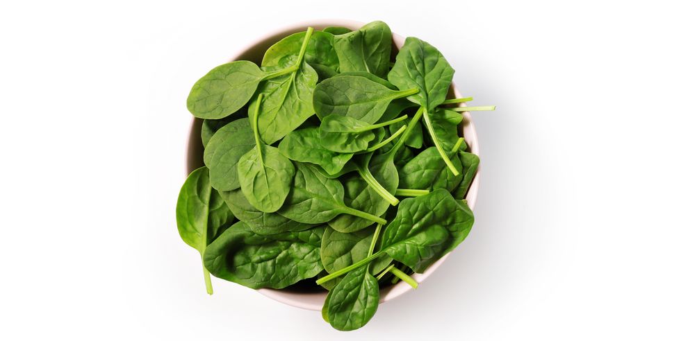 close up of spinach in bowl on white background
