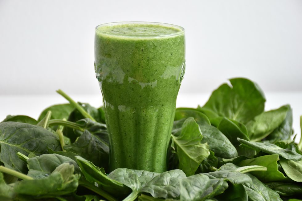 close up of spinach smoothie with vegetable over white background