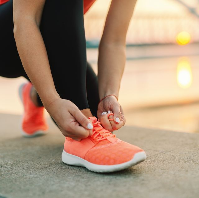 close up of sporty woman tying shoelace while kneeling outdoor in background bridge fitness outdoors concept