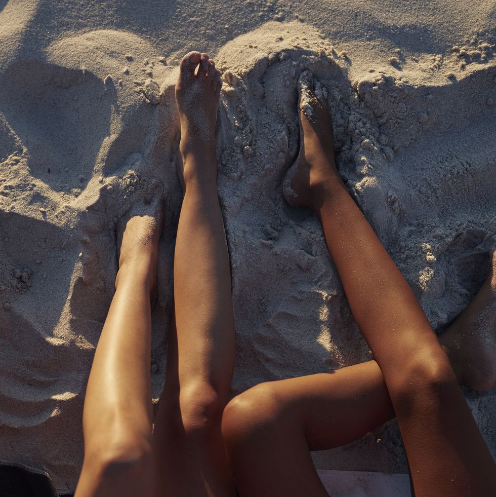Close-up of three young womens legs, on sandy beach