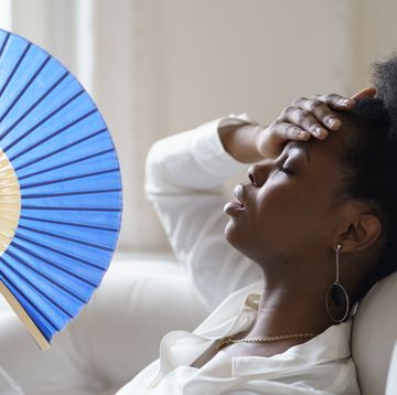 close up of tired woman holding hand fan at home