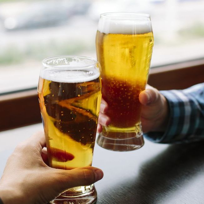 close up of two men's hands holding beer glasses