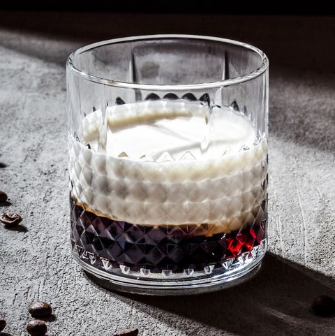 closeup of white russian in glass by roasted coffee beans on concrete table