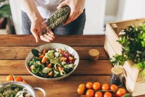 bowl met gezonde salade, vrouw voegt er pompoenpitten aan toe