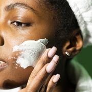 close up of woman applying cream on face while standing against green background