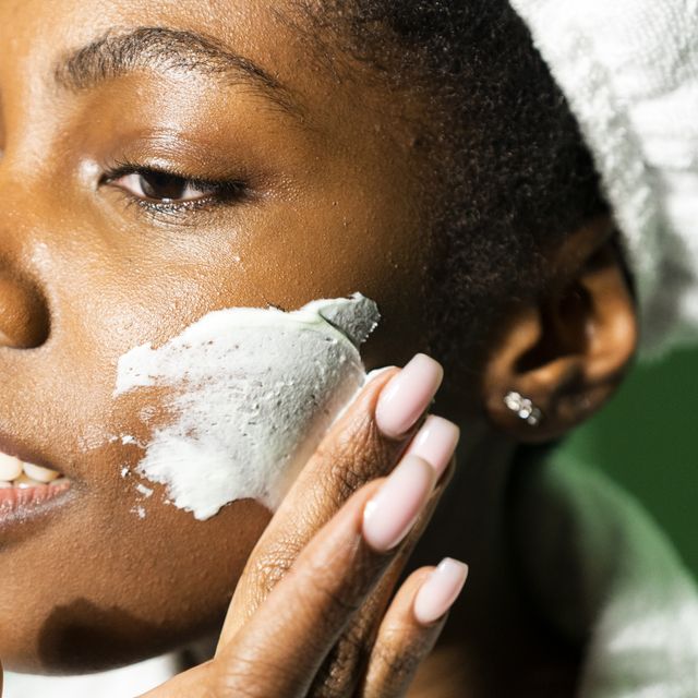 close up of woman applying cream on face while standing against green background