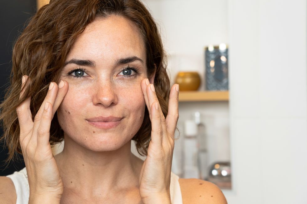 close up of woman applying cream to her cheeckbones using both hands