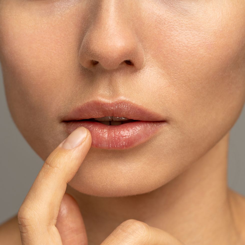 close up of woman applying moisturizing nourishing balm to her lips with her finger to prevent dryness and chapping in the cold season