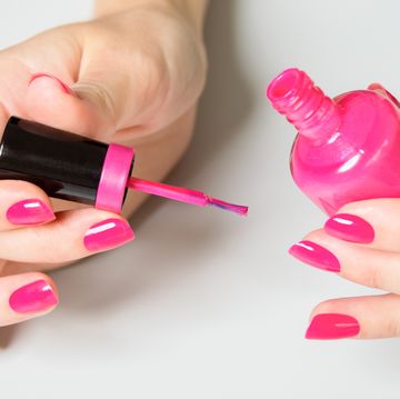 Close-Up Of Woman Applying Pink Nail Polish Against White Background