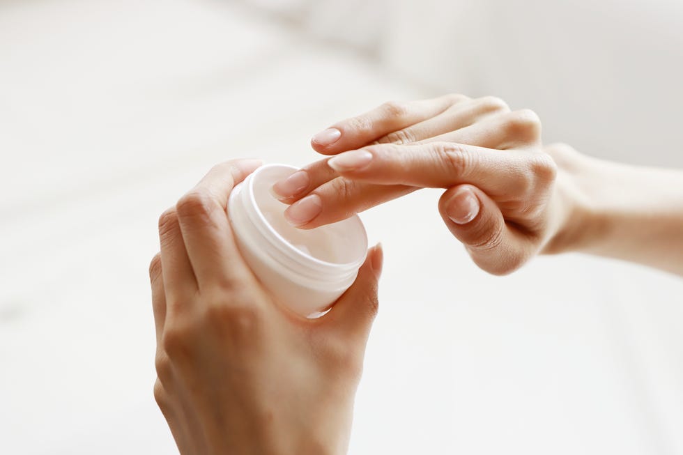 close up of woman dipping finger in cream jar