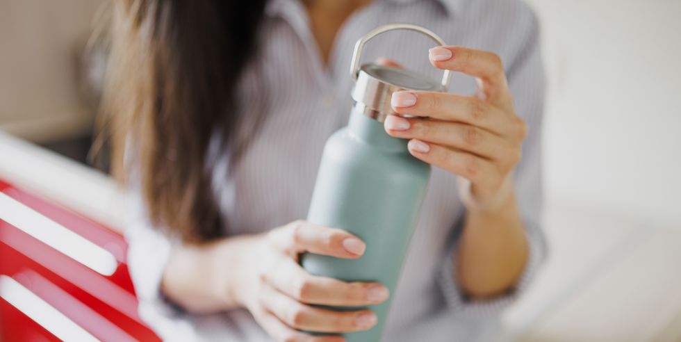 close up of woman drinking water from reusable water bottle in kitchen