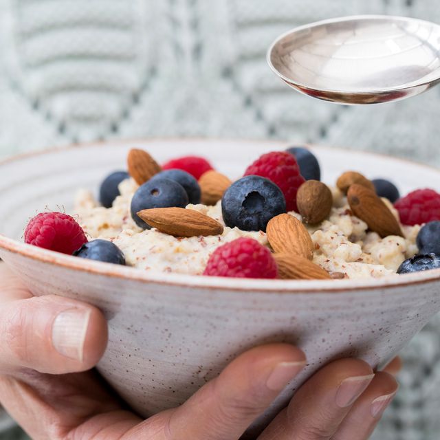 Close Up Of Woman Eating Bowl Of Porridge with Fruit And Nuts For Healthy Breakfast