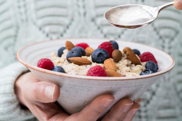 Close Up Of Woman Eating Bowl Of Porridge with Fruit And Nuts For Healthy Breakfast