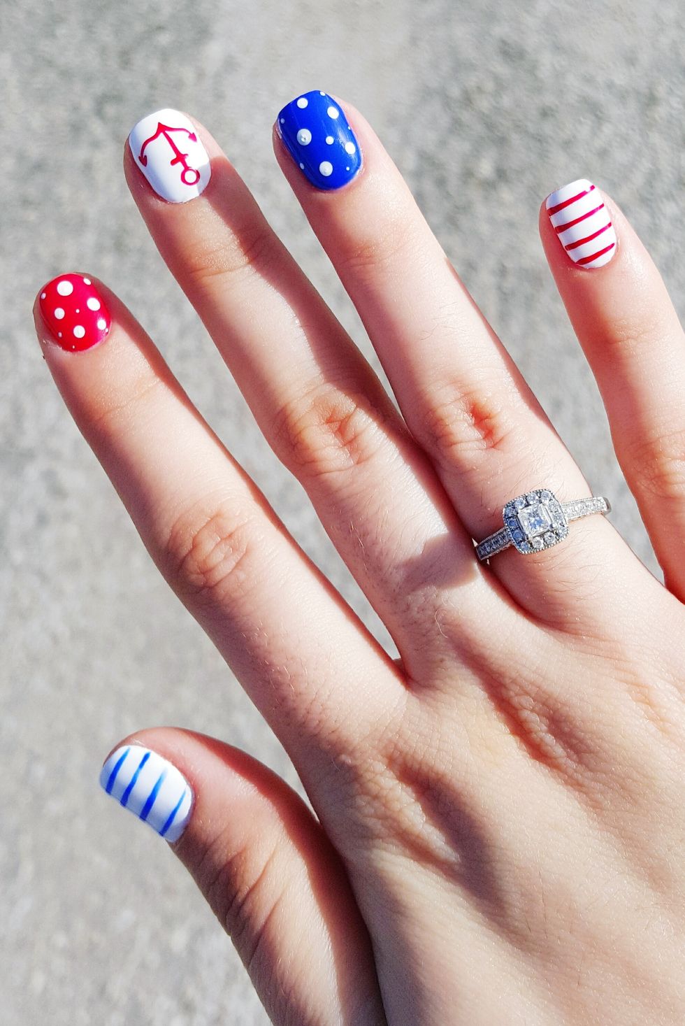 nails that feature different designs on each fingernail, like blue stripes on a white base, white polka dots on a red base, a red anchor on a white base, white dots on a blue base, and red lines on a white base