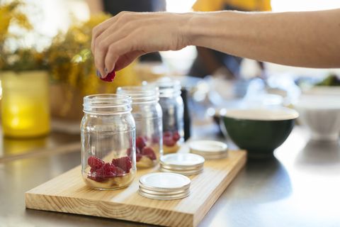 close up of woman in kitchen putting raspberry into jar