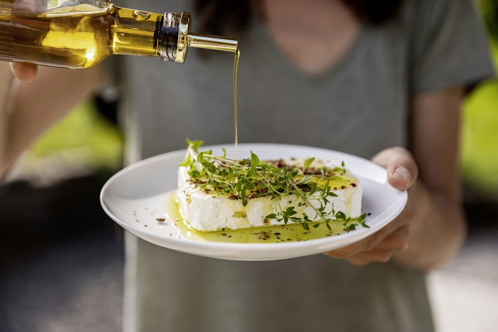 close up of woman pouring olive oil over sheep cheese on plate