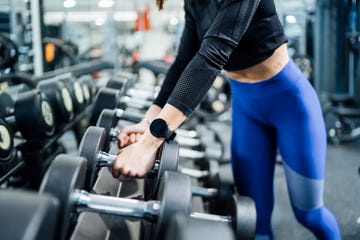 close up of woman taking dumbbells from rack in gym