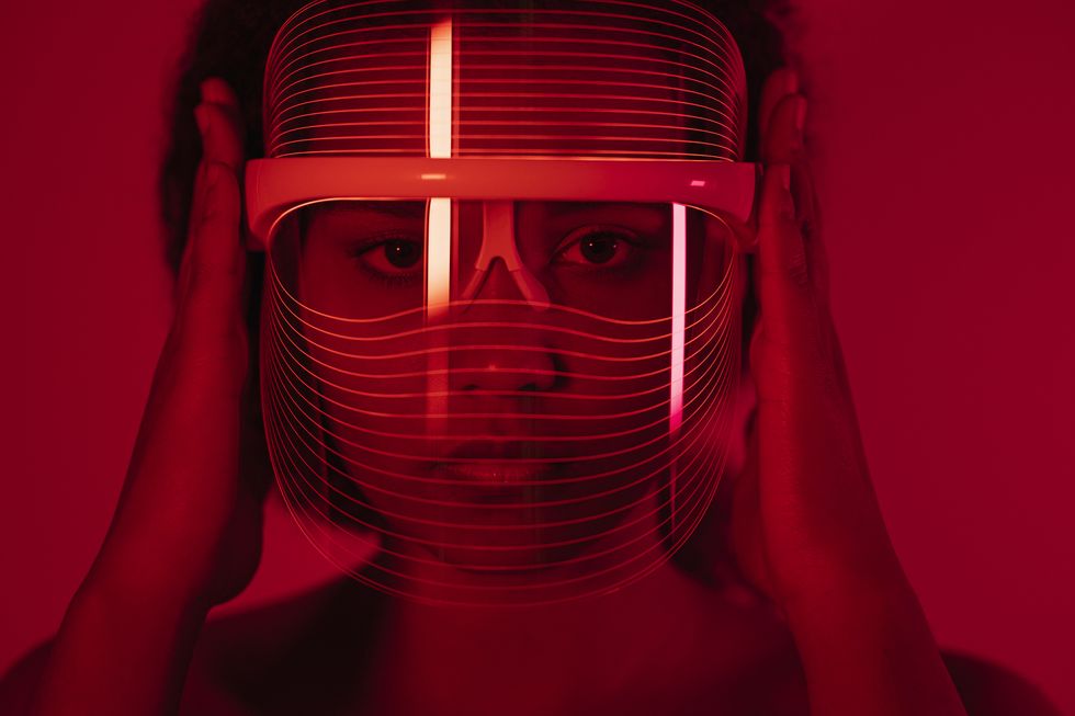 woman wearing red light therapy mask against wall at home