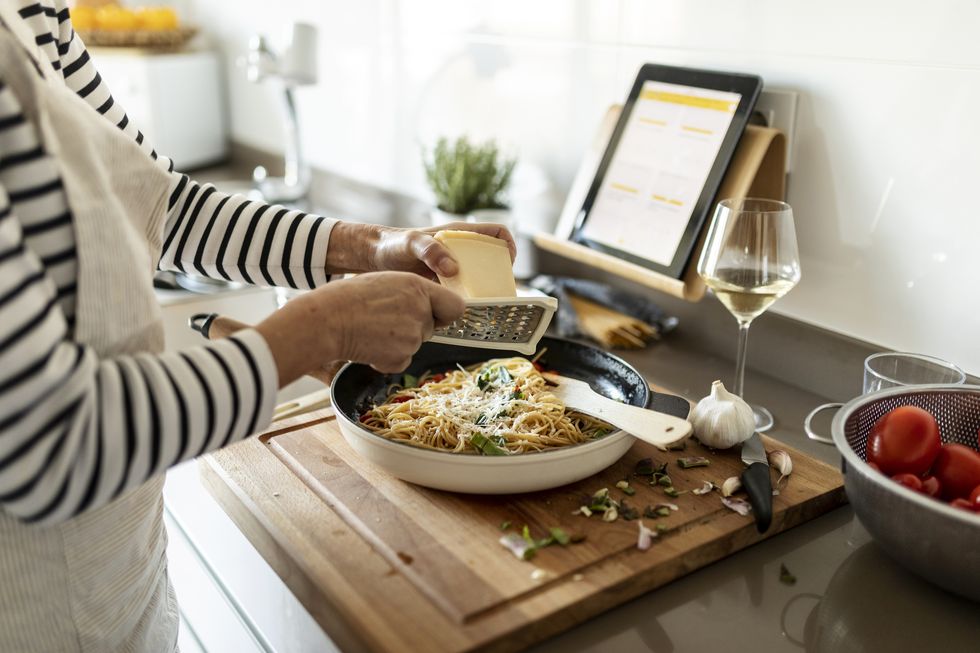close up of woman with tablet cooking pasta dish in kitchen at home