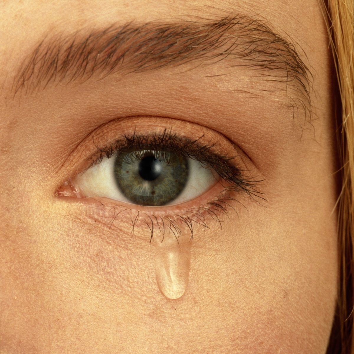 Close-up of woman's face with teardrop falling from eye