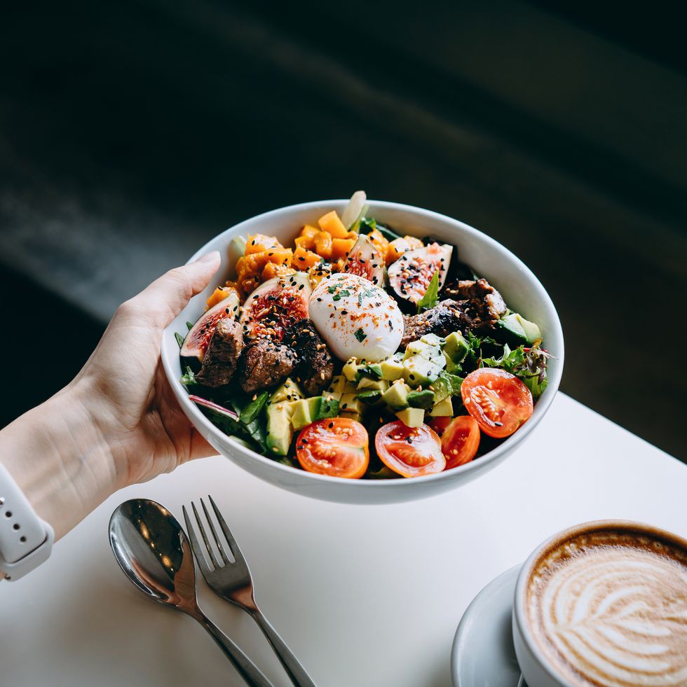 close up of woman's hand holding a bowl of fresh beef cobb salad, serving on the dining table ready to enjoy her healthy and nutritious lunch with coffee maintaining a healthy and well balanced diet healthy eating lifestyle