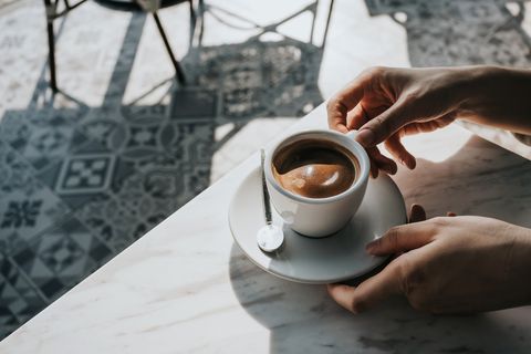 close up of woman's hand holding a cup of coffee, drinking coffee in outdoor cafe against beautiful sunlight, having a relaxing moment enjoying life's simple pleasures