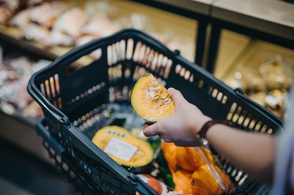 Close up of woman's hand putting fresh produce into shopping cart while grocery shopping in supermarket