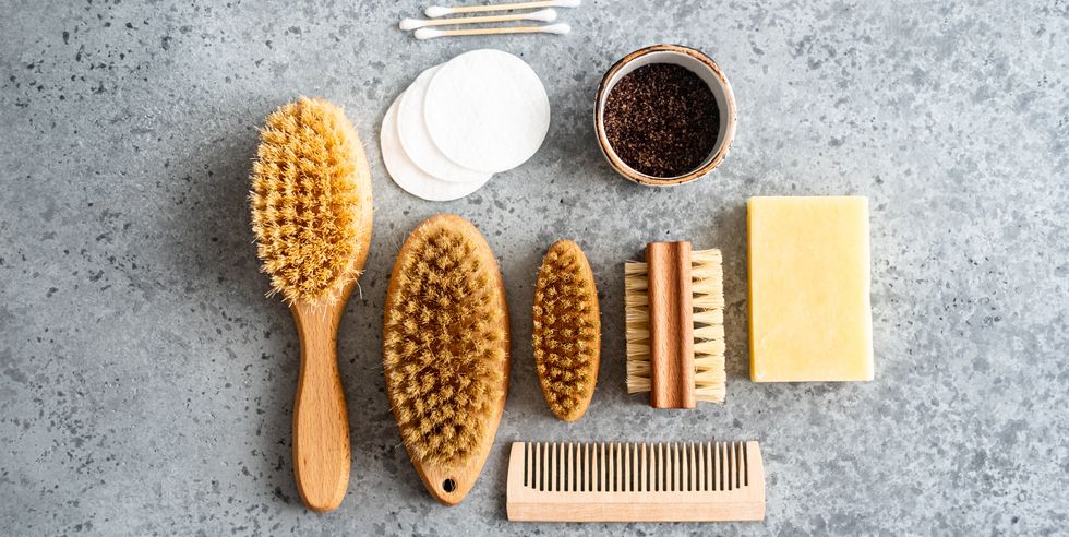 close up of wooden dry skin body brushes, bamboo tooth brushes, hair brushes, nail brush, cotton swabs and pads, cup of coffee scrub and soap on concrete background, top view spa at home, flat lay zero waste concept