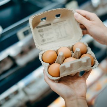 close up of young asian woman grocery shopping in a supermarket. she is holding a box of fresh organic free range eggs in front of a refrigerated section. healthy eating lifestyle
