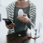 blood pressure medication recall close up of young asian woman holding a pill bottle, consulting to her family doctor online in a virtual appointment over the smartphone at home