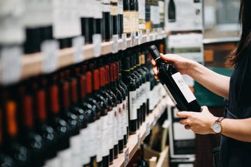 close up of young asian woman walking through supermarket aisle and choosing a bottle of red wine from the shelf in a supermarket