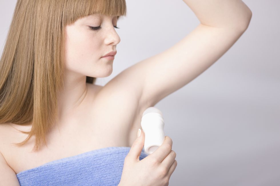 close up of young woman applying deodorant under armpits