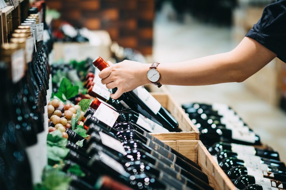 close up of young woman choosing a bottle of red wine in a supermarket