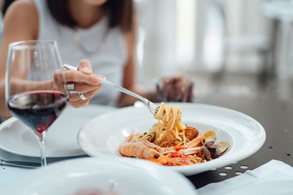 close up of young woman eating fresh seafood pasta in restaurant