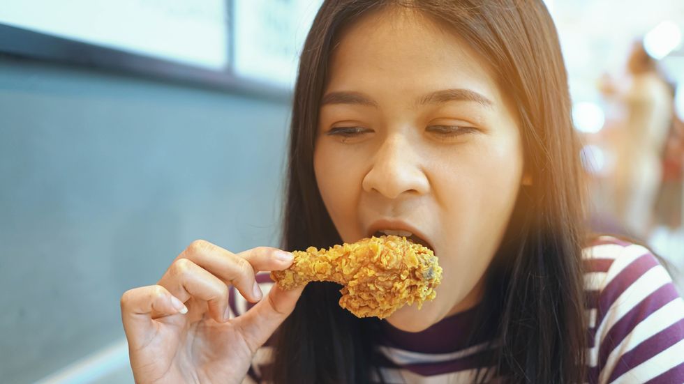 close up of young woman eating fried chicken sitting at restaurant