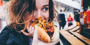 close up of young woman eating hot dog on street