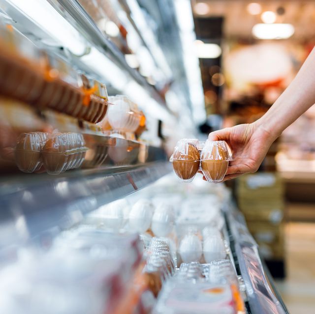 close up of young woman grocery shopping in supermarket she is holding a box of fresh organic free range eggs in front of refrigerated section healthy eating lifestyle