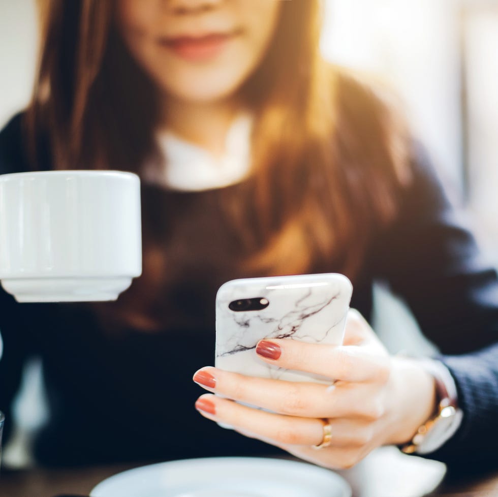 Close up of young woman having coffee and reading news on mobile phone in the early morning before work