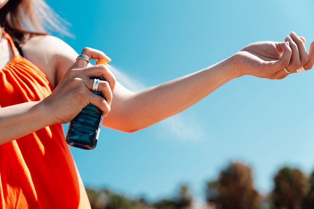 close up of young woman spraying sun cream on her arm on a sunny day