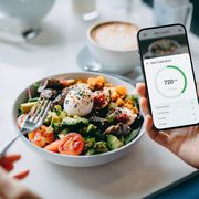 close up of young woman using fitness plan mobile app on smartphone to tailor make her daily diet meal plan, checking the nutrition facts and calories intake of her beef cobb salad maintaining a balanced diet healthy eating lifestyle