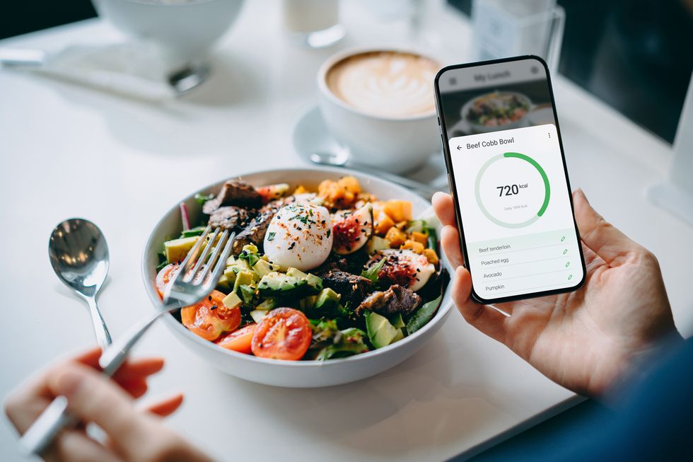 Close-up of a young woman using the fitness plan mobile app on her smartphone to make a daily diet meal plan, check the nutritional content and calorie intake of Beef Cobb Salad and maintain a healthy diet of balanced meals