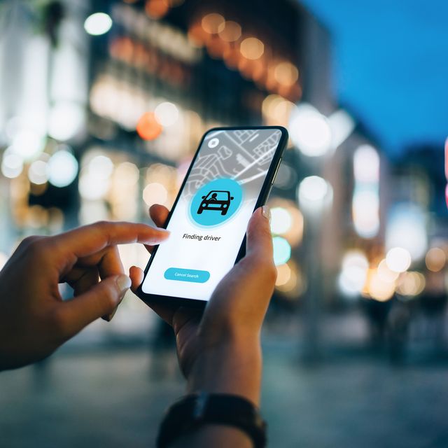close up of young woman using mobile app device on smartphone to arrange a taxi ride in downtown city street, with illuminated city traffic scene as background
