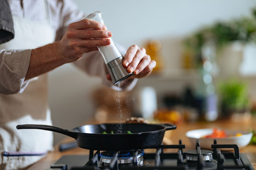 close up photo of manâs hands putting salt in frying pan at home