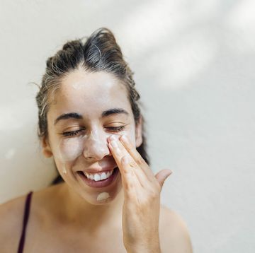 a close up portrait of a young, happy hispanic woman applying sunscreen to her cheeks and forehead