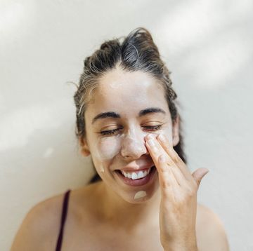 a close up portrait of a young, happy hispanic woman applying sunscreen to her cheeks and forehead