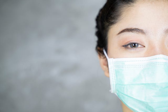 close up portrait of young asian woman with medicine health care mask against grey room background