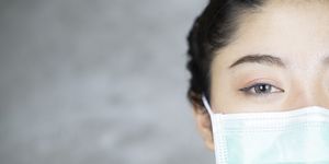 close up portrait of young asian woman with medicine health care mask against grey room background