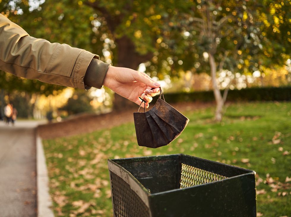 close up shot of a hand throwing a protective mask into the trash in a park on a sunny day