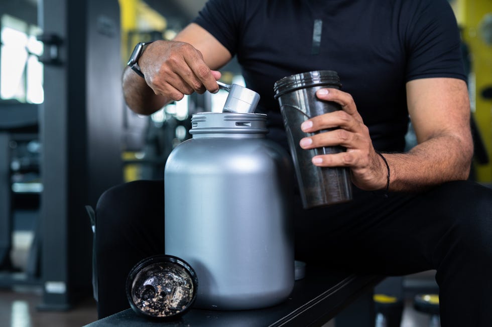 close up shot of bodybuilder hands taking protein powder and mixing with water on bottle by shaking at gym concpet of muscular gain, nutritional supplement and wellness