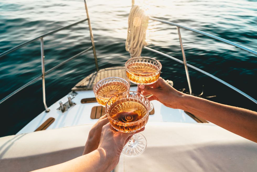 a close up shot of friends clinking sparkling wine glasses at sunset on a yacht